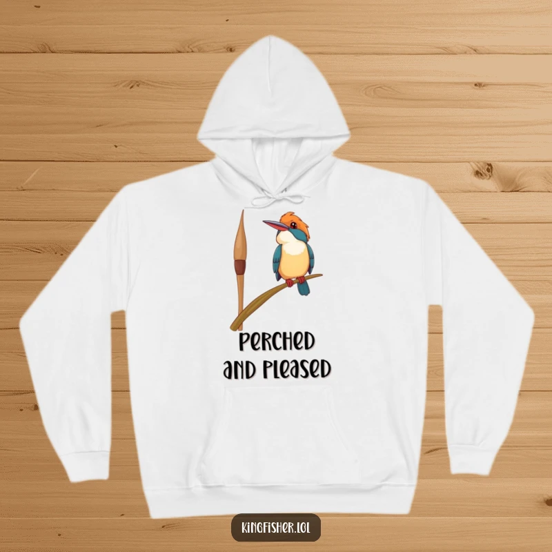 Funny happy kingfisher bird hoodie, precariously perched on a swaying reed, looking upwards with a smile, providing cozy warmth and cheerful humor.
